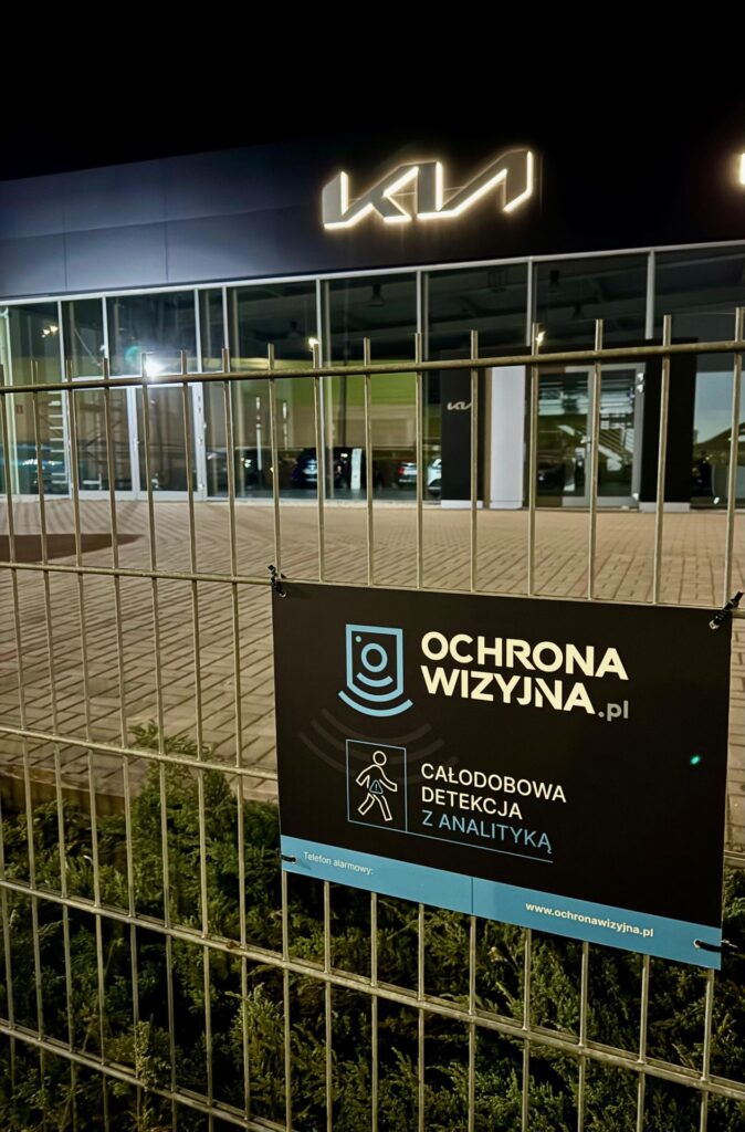 Obraz salonu samochodowego nocą z widoczną informacją, że obiekt jest chroniony monitoringiem wizyjnym